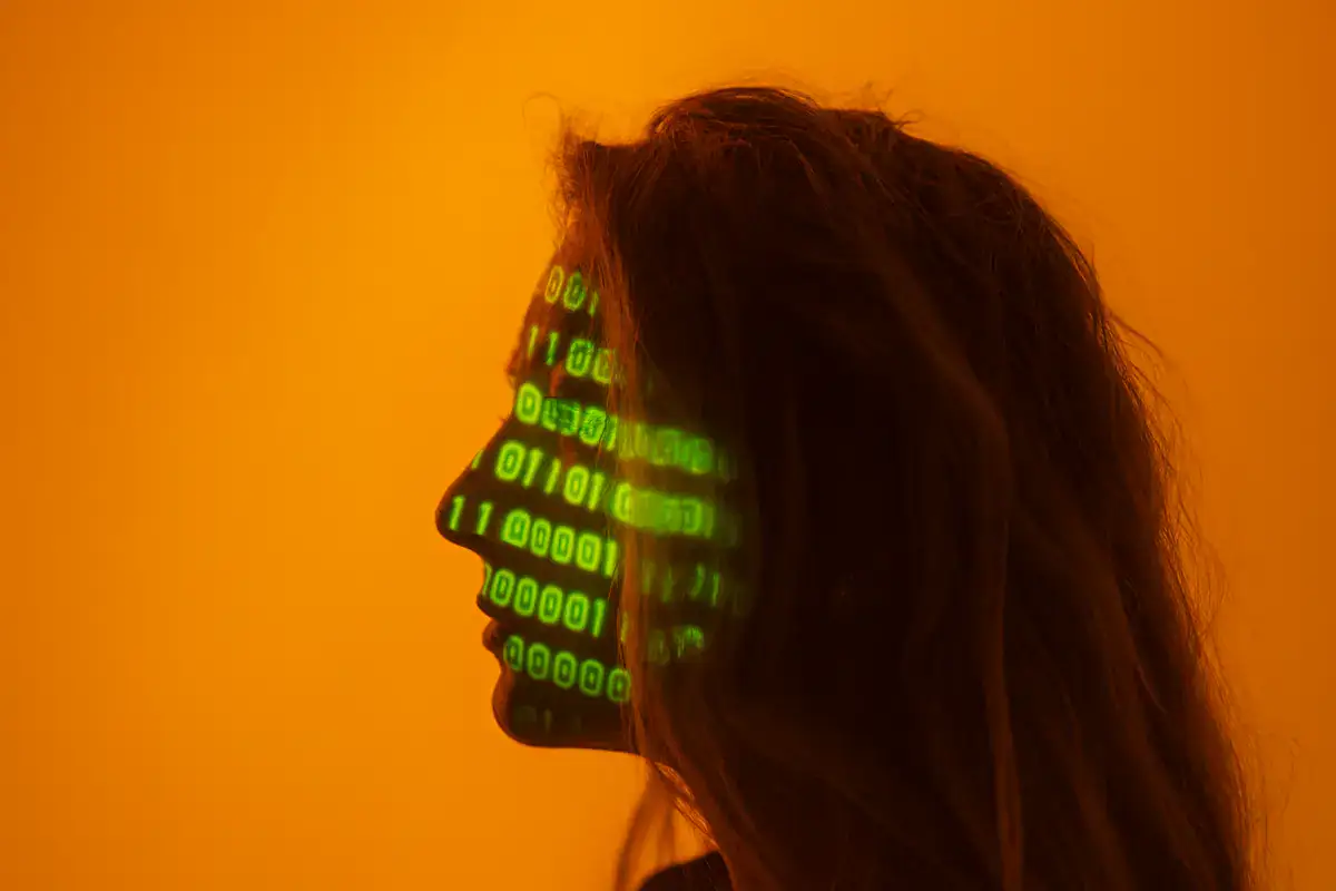 truffe online, profilo femminile con codice binario verde proiettato sul volto su sfondo arancione.