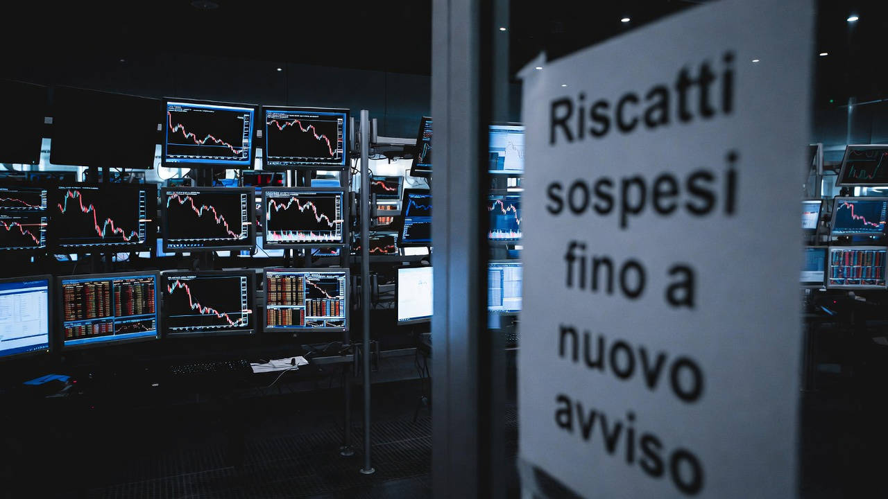 Fondi di private credit: sala trading con monitor in rosso e cartello "Riscatti sospesi fino a nuovo avviso"