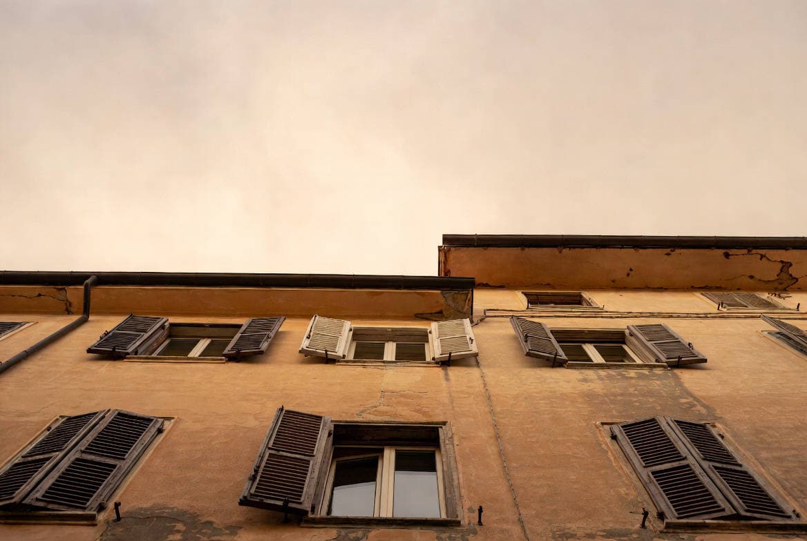 Direttiva case green edifici esistenti: facciata italiana d'epoca con persiane in legno deteriorate e intonaco scrostato, vista dal basso verso il cielo coperto