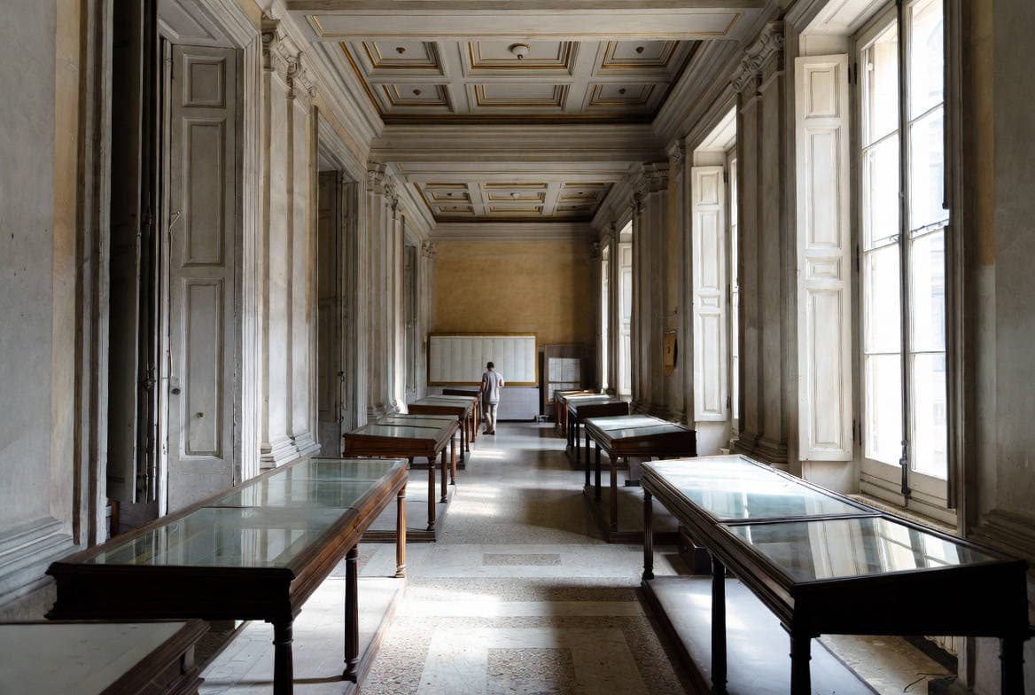 Gestione privata dei beni culturali: sala espositiva vuota di palazzo storico italiano con teche in vetro e figura di spalle