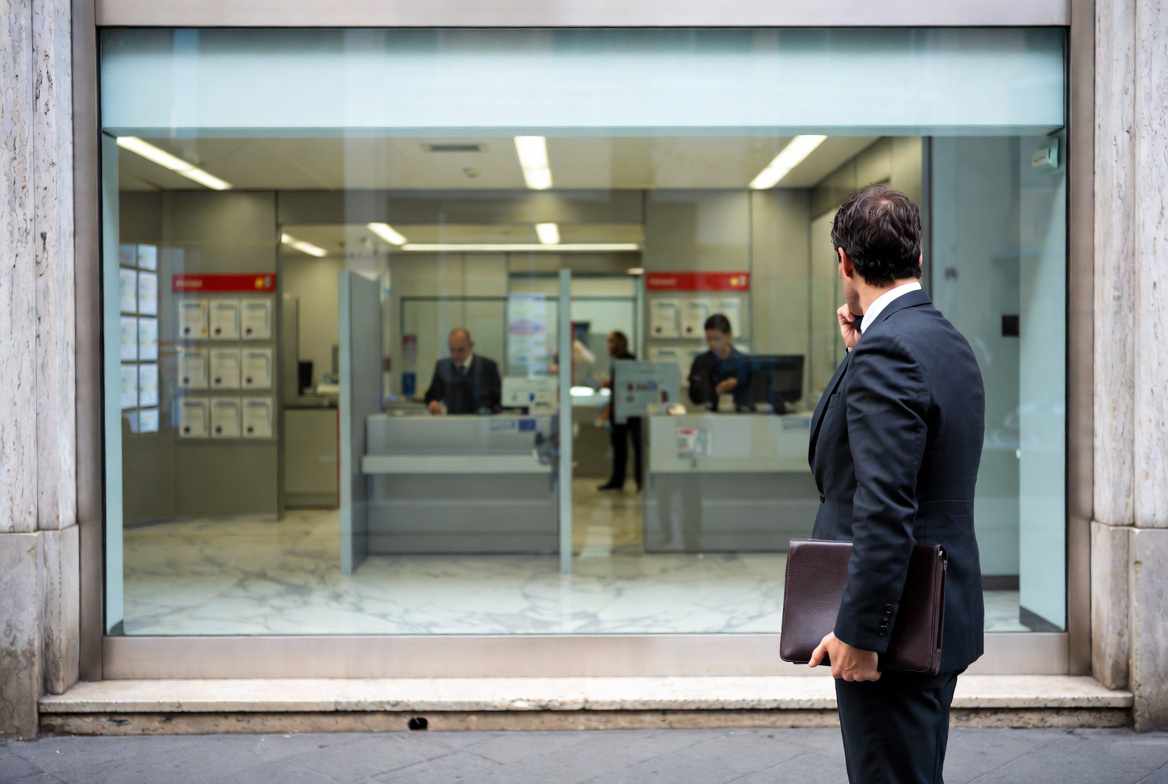 Reti terze credito: professionista indipendente davanti a una filiale bancaria vuota