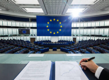 Savings and Investments Union: emiciclo del Parlamento europeo vuoto con bandiera UE e documenti finanziari in primo piano