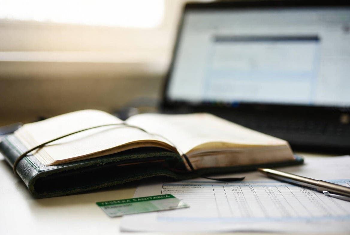 Spese sanitarie senza scontrino: tessera sanitaria, agenda e documenti fiscali su una scrivania con laptop sullo sfondo