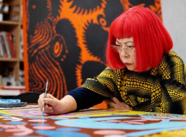 Yayoi Kusama dipinge nel suo studio, con parrucca rossa e abito a pois gialli e neri.