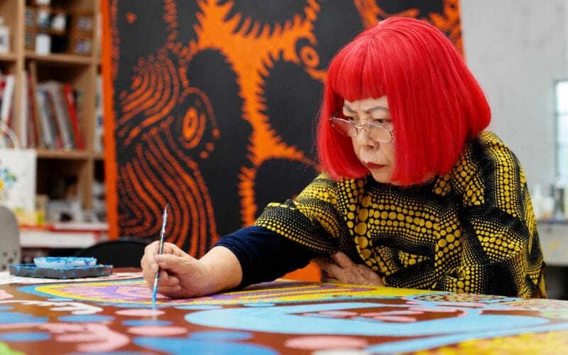 Yayoi Kusama dipinge nel suo studio, con parrucca rossa e abito a pois gialli e neri.