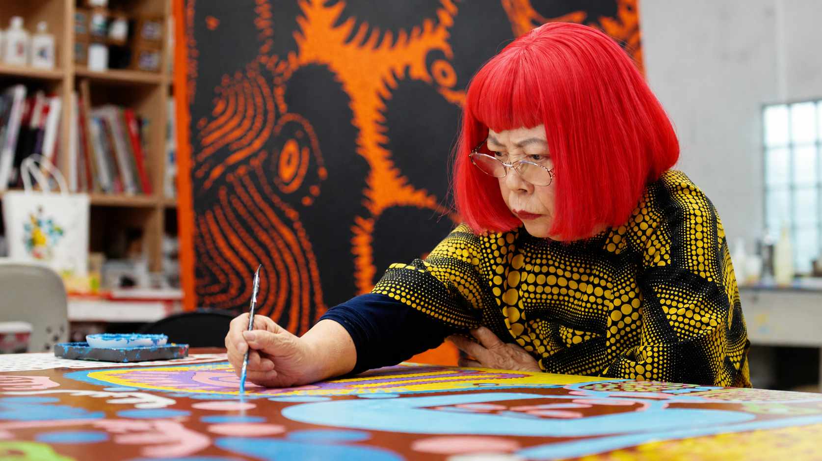 Yayoi Kusama dipinge nel suo studio, con parrucca rossa e abito a pois gialli e neri.