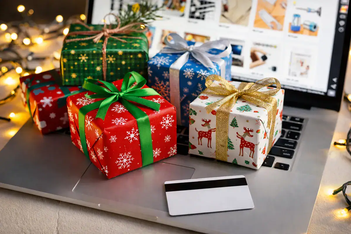 Truffe online a Natale: nel 2025 lo shopping diventa un campo minato digitale. Truffe online a Natale con pacchi regalo colorati su laptop aperto, carta di credito in primo piano e luci natalizie che richiamano lo shopping digitale festivo.